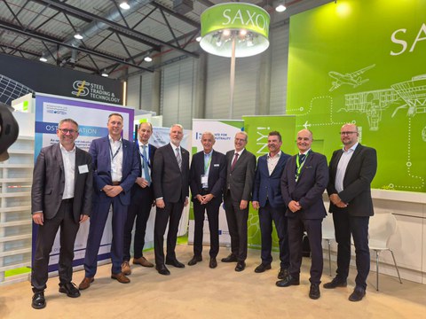 Gruppenfoto: neun Männer stehen nebeneinander auf der ILA Berlin auf einem Stand und lächeln in die Kamera.