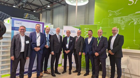 Gruppenfoto: neun Männer stehen nebeneinander auf der ILA Berlin auf einem Stand und lächeln in die Kamera.