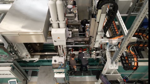 Eine Maschine wird von oben fotografiert. Es stehen zwei Arbeit an der Anlage und arbeiten.