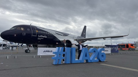 Two men stand in front of a Lufthansa aircraft. In front of them is a three-dimensional "ILA" letter installation.
