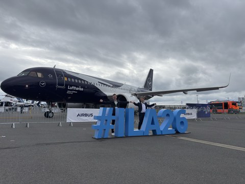 Two men stand in front of a Lufthansa aircraft. In front of them is a three-dimensional "ILA" letter installation.