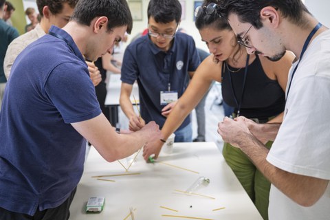 Studtent:innen stehen um einen Tisch, auf dem Spaghetti liegen und beraten sich.
