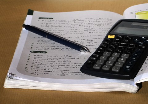 Geööfnetes Mathebuch mit darin liegendem Stift und Taschenrechner
