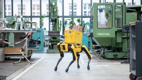 Robo-Dog steht mit einer Post-Box auf dem Rücken in der Versuchshalle des LWM