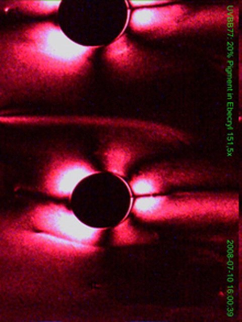 Polarisationsmikroskopische Aufnahme einer nematischen Suspension (etwa 200 nm lange Pigmentkristallite in einem apolaren Lösungsmittel) mit flussinduzierten Texturen des Direktorfeldes um Lufteinschlüsse.