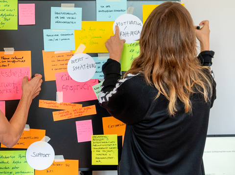 Eine Kollegin pinnt Post-Its an eine Wand.