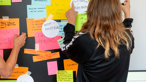 Eine Kollegin pinnt Post-Its an eine Wand.