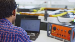 Wissenschaftler sitzt am PC im Labor, im Hintergrund ein autonomer Feldroboter