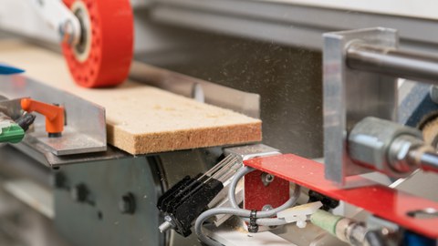 Die Abbildung zeigt den Auschnitt aus der FALSA-Anlage, in der eine Drehvorichtung den abgetrennten Streifen aus Holzfaserwerkstoff neu ausrichtet.