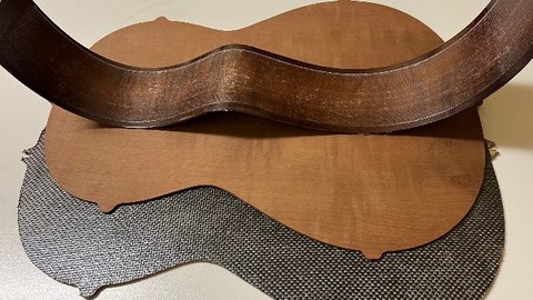 Im Bild sind die Gitarrenbauteile Boden und Zarge einer Konzertgitarre zu sehen. Diese sind mit einem textilen Faserhalbzeug verstärkt.