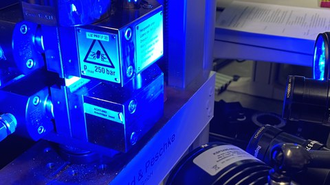 Im Bild ist ein Messaufbau zur Druckprüfung an Holzproben mit einem optischen Messsystem zu sehen.