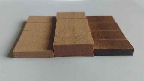 Das Bild zeigt drei Holzproben nach einer Wasserlagerung: links natives Buchenholz, in der Mitte nativ verdichtetes Buchenholz mit größerer Quellung und rechts eine verdichtete Probe mit dunklerer Färbung