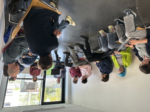 DAs Bild zeigt einen Arbeitkreis - eine Gruppe von 11 Menschen sitzt im Halbkreis und diskutiert.
