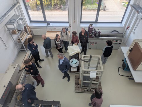 Das Bild zeigt von schräg oben 11 menschen, die sich in einem Technikum eine Furnierschälmaschine anschauen