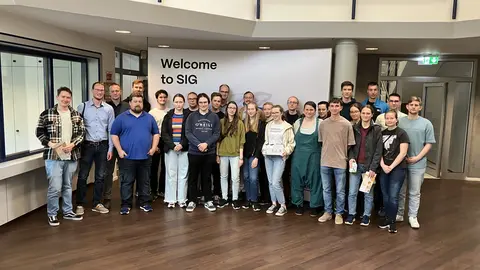 Foto einer der Exkursiongruppe vor einem Banne mit der Aufschrift Welcome to SIG