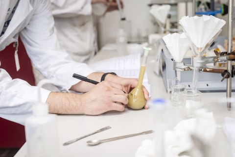 Das Foto zeigt die Hände einer Person im Labor, die einen Chemikalienbehälter beschriftet.
