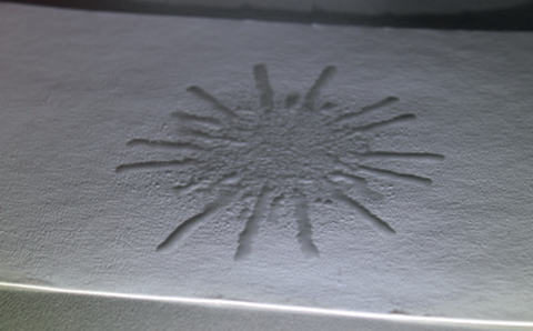 Foto von Wasserstropfen in sternförmigen Muster auf einer weißen Kartonoberfläche.