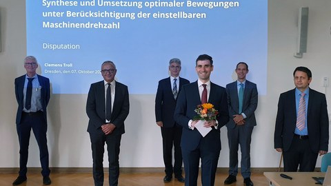 Foto von Clemens Troll und der Promotionskommission. Im Hintergund der Titel "Synthese und Umsetzung optimaler Bewegungen unter Berücksichtigung der einstellbaren Maschinendrehzahl"