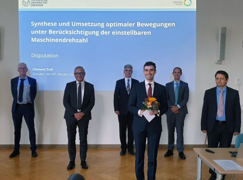 Foto von Clemens Troll und der Promotionskommission. Im Hintergund der Titel "Synthese und Umsetzung optimaler Bewegungen unter Berücksichtigung der einstellbaren Maschinendrehzahl"