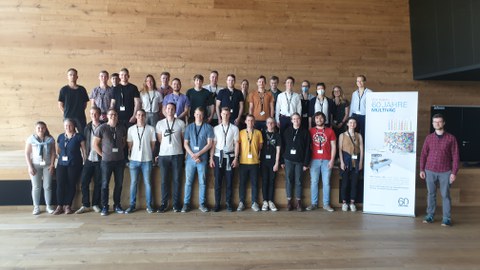 Gruppenfoto mit ca. 30 Personen vor einer Wand aus Holz mit einem Aufsteller "60 Jahre Musltivac".