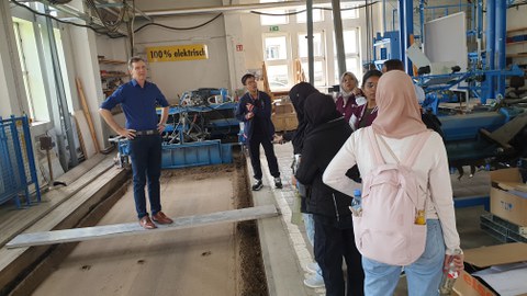 Studierende im einer Industriehalle. Ein Mann steht auf einem Brett.