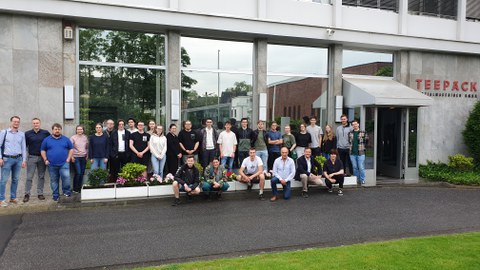 Gruppenfoto von ca.30 Personen vor einem Gebäude mit der Aufschrift Teepack.