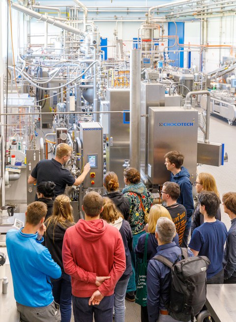 Studirende schauen eine Produktionasanlage aus Edelstahltanks und Rohren an. 