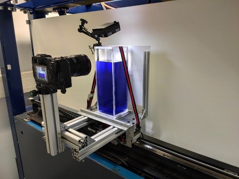 Foto of test rig for investigating intermittent fluid transport. A fluid-filled container is installed on a linear direct drive. A camera records the behavior of the fluid surface during a test.