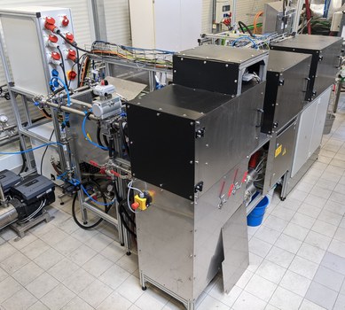 Foto einer Versuchsanlage bestehend aus Rohren, Kabeln und drei mit Metall verkleideten Kästen.