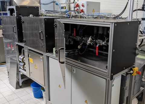 Foto einer Versuchanlage mit drei metallverkleideten Kästen. Ein kasten ist geöffnte und gibt den Blick auf Rohre und Hebel frei.