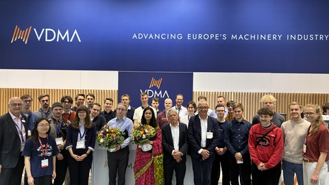 Gruppenfoto mit ca. 30 Personen. In der ersten Reihe halten zwei Personen große Blumensträuße. 
