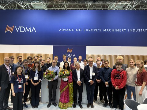 Gruppenfoto mit ca. 30 Personen. In der ersten Reihe halten zwei Personen große Blumensträuße. 