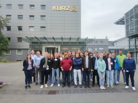 Studierendengruppe vor einem grauen Bürogebäuder mit logo der Firma Kurz.