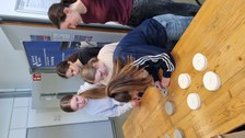 Ein Gruppe Mädchen steht an einem Tisch. Ein Mädhcen beschriftet eine Kartonprobe.