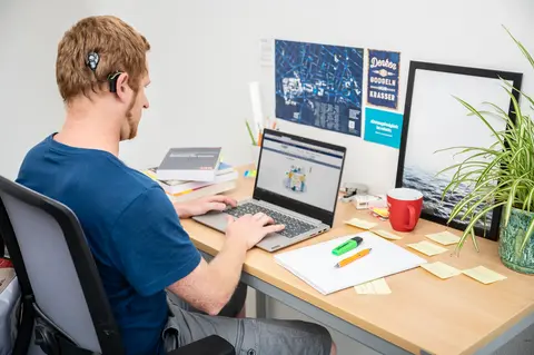 Photo of a student with hearing aid. He is sitting at a desk in front of his notebook.