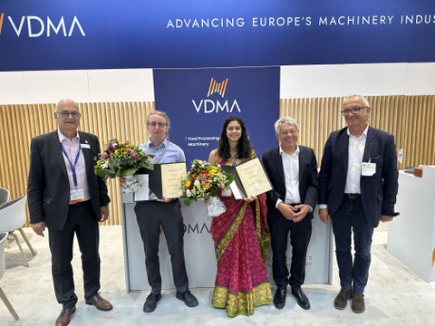 Foto von 5 Personen. Zwei Personen halten einen Blumenstrauß und eine Urkunde. Alle Lächeln in die Kamera.