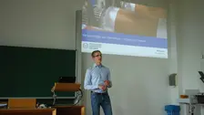 Vortragender Ludwig Schmidtchen mit Präsentation im Hintergrund.