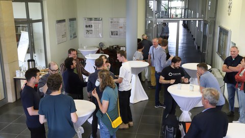 Mehrer Personen unterhalten sih an Stehtischen in einem Foyer.