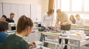 Bild von 8 Studenten, die in einem Klassenzimmer in zweier Gruppen zusammen an einem Elektroprojekt arbeiten.