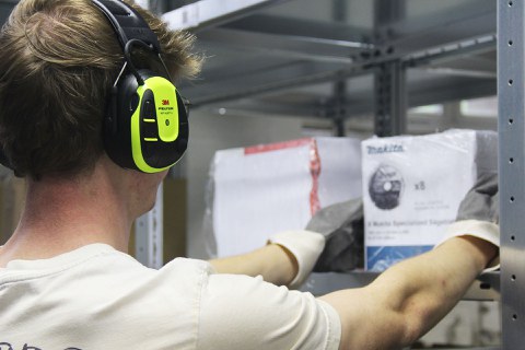 Foto eines Lageristen, der ein Headset trägt und eine Kiste in ein Regal einlagert.