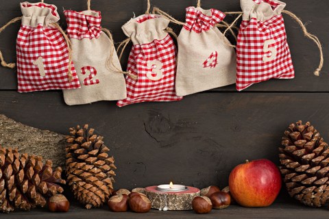 Foto von 5 hängenden Weihnachtsbeuteln, einer leuchtenden Kerze mit Kastanien, einem Apfel und Tannenzapfen