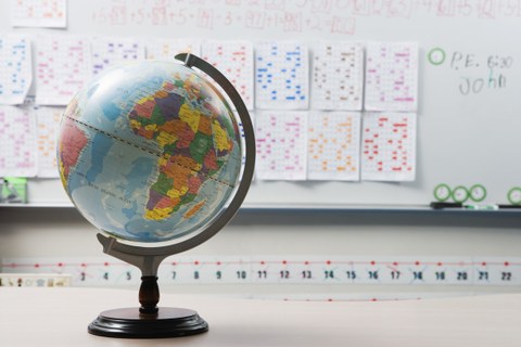 Das Foto zeigt einen Globus. Im Hintergrund befinden sich viele Zettel mit farbigen Markierungen an einem Whiteboard.