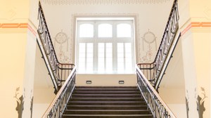 Foto: repräsentatives Haupttreppenhaus des Zeuner-Baus, des Hauptgebäudes der Fakultät Maschinenwesen. Blick von unten, auf das Halbpodest mit großem Fenster. Das Treppenhaus ist ausgestattet mit historischer Malerei und schmiedeeisernem Geländer. 