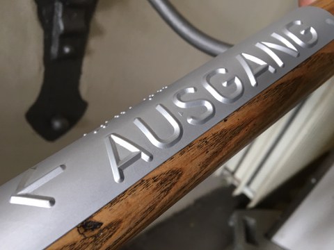 Foto: Detailaufnahme eines Handlaufschildes aus Aluminium, auf dem das Wort Ausgang in Braille und erhabener Pyramidenschrift und ein Pfeil zu sehen ist.