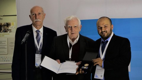 Das Foto zeigt Prof. Heinz Linke, der die Fritz-Kesselring-Ehrenmedaille und eine Urkunde in den Händen hält. Neben ihm stehen zwei Männer.