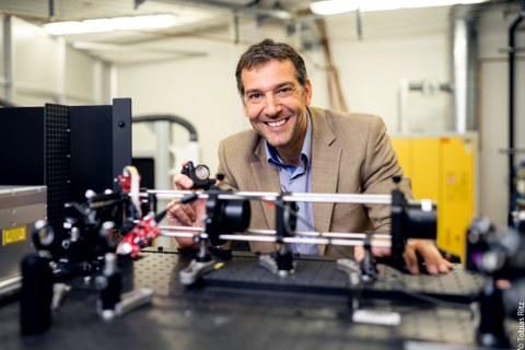 Der internationale Laserexperte Prof. Andrés Lasagni steht hinter seinem Laser. Der Laser ist flach und steht auf einer Platte.