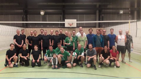 Auf dem Foto sieht man das Gruppenbild von Sportlern, die sich in einer Turnhalle vor einem Volleyballnetz in drei Reihen aufgestellt haben.