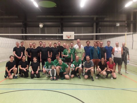 Auf dem Foto sieht man das Gruppenbild von Sportlern, die sich in einer Turnhalle vor einem Volleyballnetz in drei Reihen aufgestellt haben.