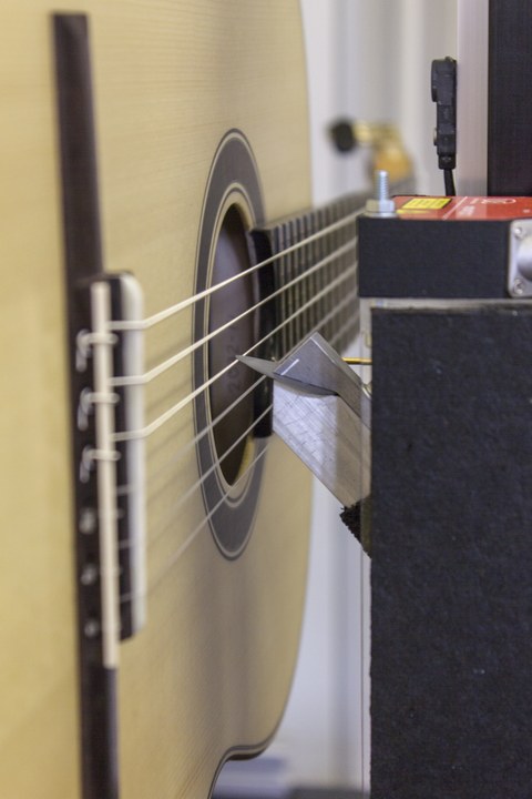 Detailaufnahme von Gitarrensaiten, die gerade von einer Testvorrichtung angezupft werden.