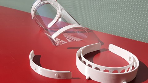 Das Foto zeigt drei Beuteile einer Gesichtsschutzmaske, die im 3D-Drucker gefertigt wurden. Die Teile liegen auf einem roten UNtergrund.